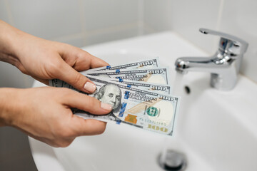 Women's hands hold money against the background of a sink and a faucet with water. Concept of utilities, payment and savings.