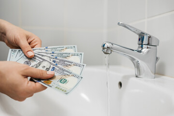 A woman holds money on a background of a sink with water. Utility estimates, repairs and plumbing repair services. Household financial expenses concept.