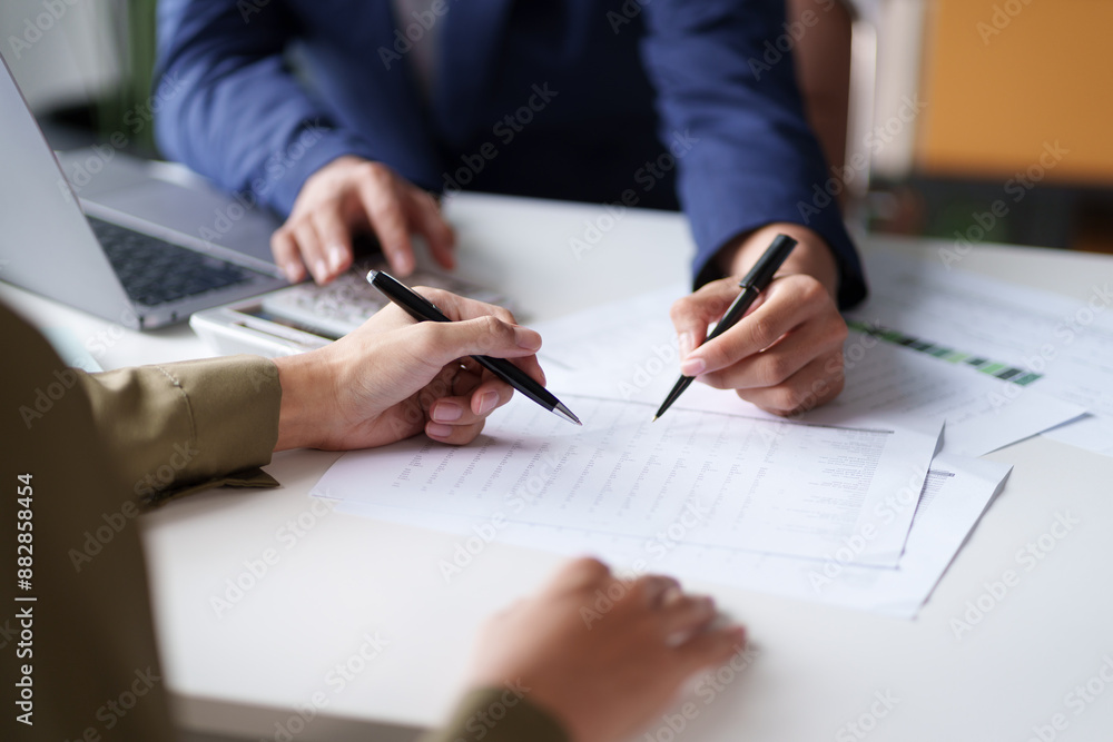Wall mural close-up of two individuals discussing and pointing at a document on a desk. the hands are holding p