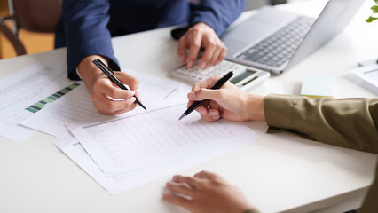 Close-up of two individuals discussing and pointing at a document on a desk. The hands are holding pens, indicating a review or collaboration on the content of the document