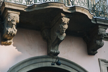 Balcony with caryatids in the form of mascarons with heads and wavy elements. Facade of an old...