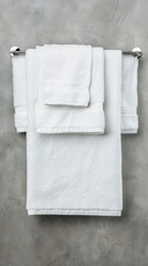 Two white towels are stacked on a white countertop in a bathroom. A white towel rack and window blinds are in the background