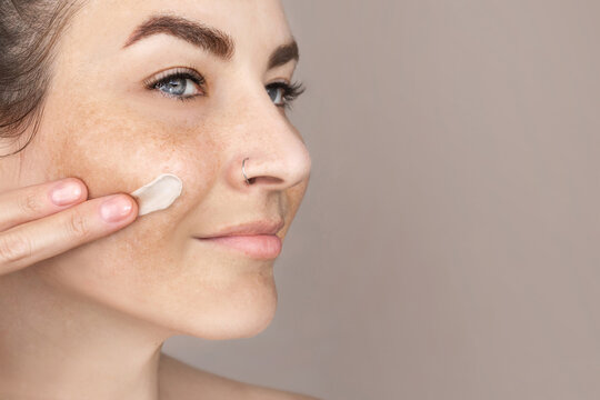 Caucasian woman's face with freckles or age spots, she smears cream on her cheek with her fingers, nice cream swatch, copy space for text
