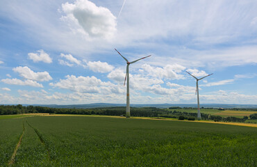 Two wind rubrines in rural landscape with fields and forest and blue sky with clouds