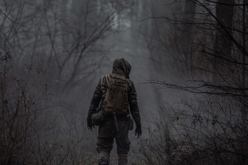 A man in camouflage in a post-apocalyptic smoky dark forest. Back view. The concept of a lone...