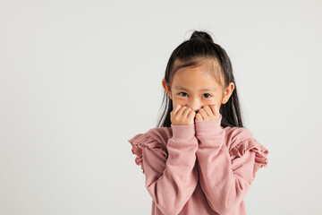 Asian portrait cute young kid girl standing amazed, shocked afraid mouth covered gesturing hand palms looking camera, studio shot isolated on white background, Thai kindergarten child scared