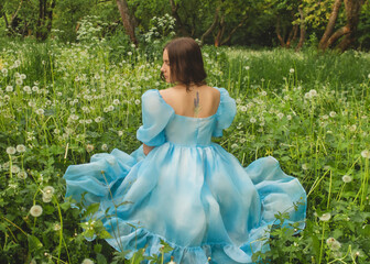 The beautiful young brunette woman in the dandelions background in the park close up in spring season.