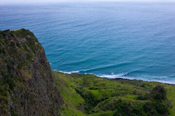 Narrow promontory rising high above over calm blue waters of Tasman Sea. Te Toto Gorge Lookout, Raglan, New Zealand