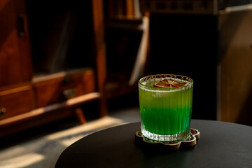 tropical brazilian mocktail with pineapple, green apple, and orange soda in a transparent glass. Served on black table in a vintage music room environment