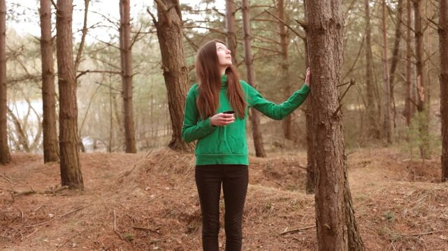 Woman meditating in a pine forest with a cup of tea. 