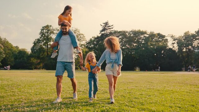 A family is relishing a warm, sunny day outdoors, walking together in a green park. Parents and kids create joyful memories, bonding and enjoying quality time