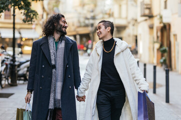 Happy gay couple holding hands while carrying shopping bags