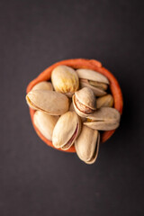 Pistachio nuts in wooden bowl on black background. Pistachios are rich in nutrients and good source of protein, fiber, and antioxidants. Healthy food concept. Flat layout.