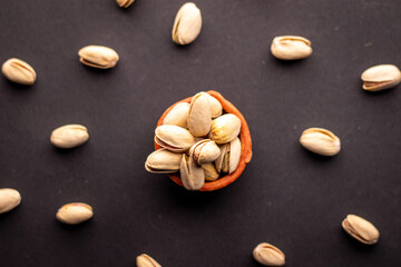 Pistachio nuts in wooden bowl on black background. Pistachios are rich in nutrients and good source of protein, fiber, and antioxidants. Healthy food concept. Flat layout.