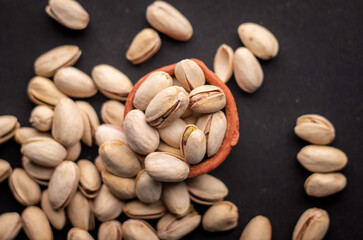 Flat lay picture of Pistachio nuts kept in a clay pot on a dark grey background