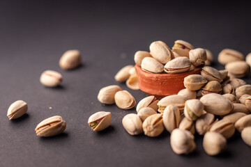 Pistachio nuts kept in a clay pot on a dark grey background with a space for text on the left