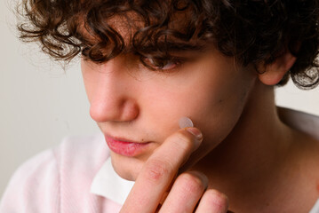 Young man uses acne stickers as bandage not to touch or squeeze pimple. Using acne pimple patch to...