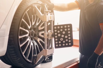 A professional technician placing sensors on a car's tires for computer-assisted wheel alignment and balance check at a car repair shop. © mohammed.imthiaz