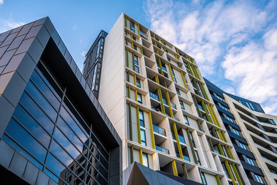 Modern urban buildings with a mix of glass and concrete facades against a partly cloudy blue sky
