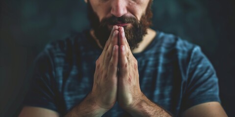 Man with beard and mustache sits in chair, hands clasped together. Dark background focuses on subject contemplative pose. Suitable for meditation, spirituality, or introspection themes.