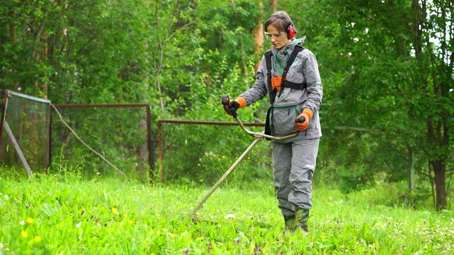 Person woman operating a weed trimmer in a lush, green outdoor setting. Wearing protective gear and focused on the task.
