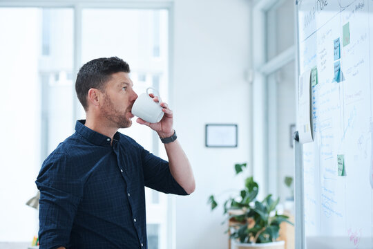 Man, drink and morning in office for brainstorming with whiteboard, thinking and planning for day ahead or creative tasks. Project manager, coffee and ideas for campaign schedule and goal setting.