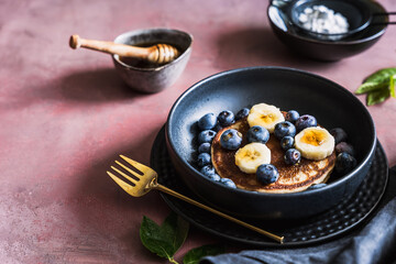 Frische Pancake mit Banane und Blaubeere auf einem schwarzen Teller. Frühstück, moody.