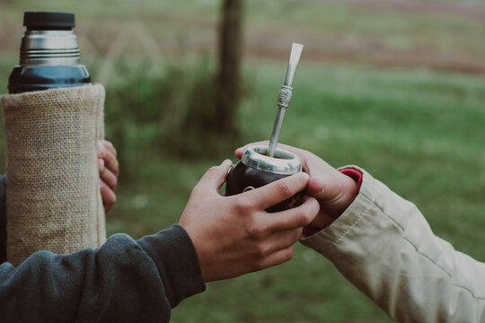 Manos j&oacute;venes compartiendo un mate en el campo.