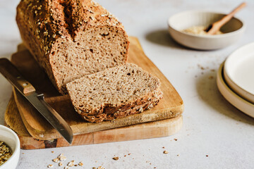 Gebackenes Vollkornbrot mit Sesam und Haferflocken aufgeschnitten auf einem Holz Schneidebrett. Nahaufnahme, hell.