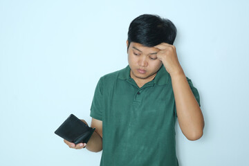Young Asian man showing expression sad and confused face while looking at his wallet. Wearing a green t-shirt