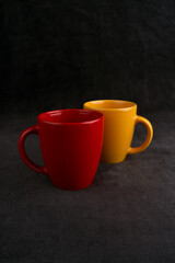 Coffee or tea cups on black texture background. Yellow mug. Red glass. Corporate colors. ceramic mugs