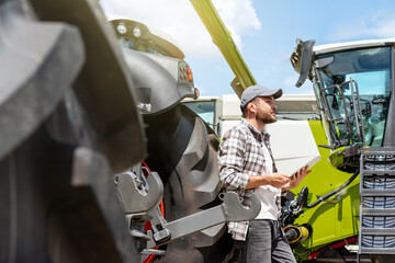 Sale of agricultural machinery. A man with a digital tablet leans on the wheel of a farm tractor. © Barillo Images