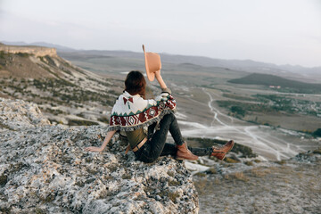 serene woman in hat sits atop mountain, gazing at sprawling valley below