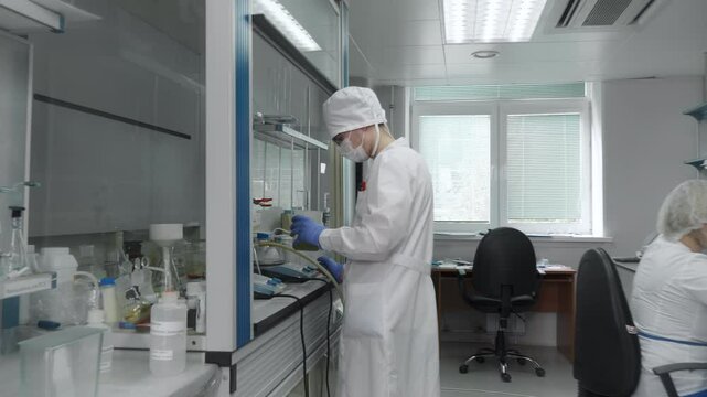 Multiple Medical Workers operating in the Medical Laboratory. A Male laborant shakes the Plastic Container with Liquid Substance. Slowly Pouring the Fluid into the Beaker. Medical Production Process.
