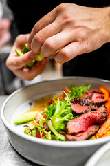Close-up of hands garnishing a gourmet dish with greens, highlighting the culinary art and fresh ingredients