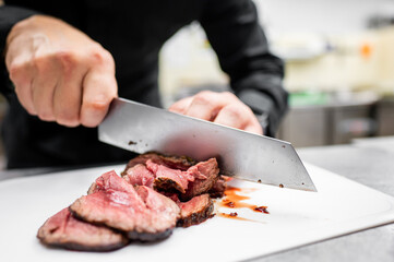 A chef’s hands expertly slice cooked steak on a white plate using a large knife