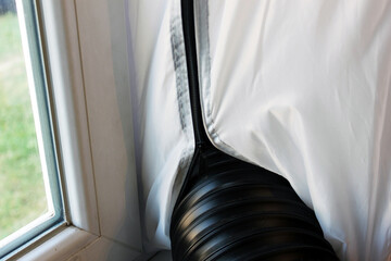 Portable air conditioner exhaust hose venting hot air outside through window with plastic cover