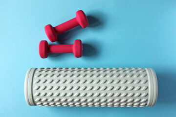 Pink dumbbells are lying near foam roller on blue background, promoting healthy lifestyle and active hobbies