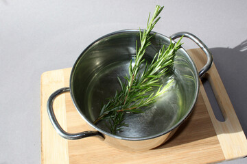 Sprig of fresh rosemary infusing in hot water inside a metal pot, releasing its aromatic flavor and...