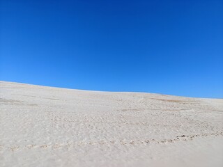 Minimalistic, empty sand dune with footprints and clear, blue sky horizon without clouds