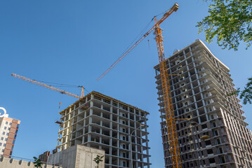 A tower construction crane next to a high-rise building under construction. The frame of the building under construction next to the crane. The structure of the building is made of reinforced concrete