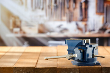 Mechanic bench vice on a wooden workbench in a craftsman's workshop. A blurred wall with tools in the background. Empty advertising space  for mounting products and objects.