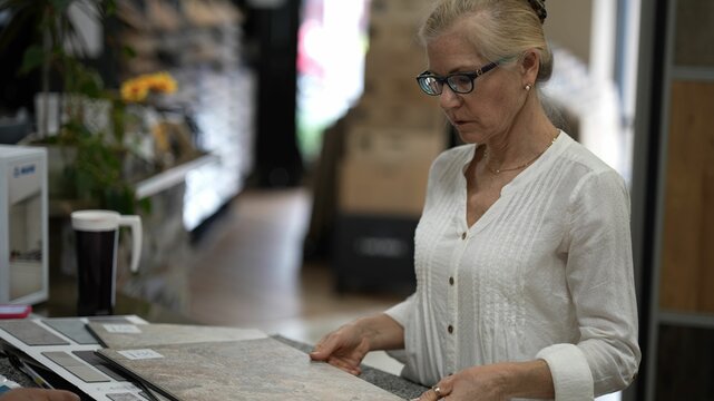Happy mature woman looking at samples of floor tiles in a store, consider using vct or engineered tile in a home renovation project.