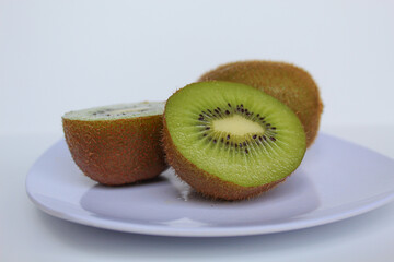 Cut and uncut kiwi fruits, on white plate, isolated on white background