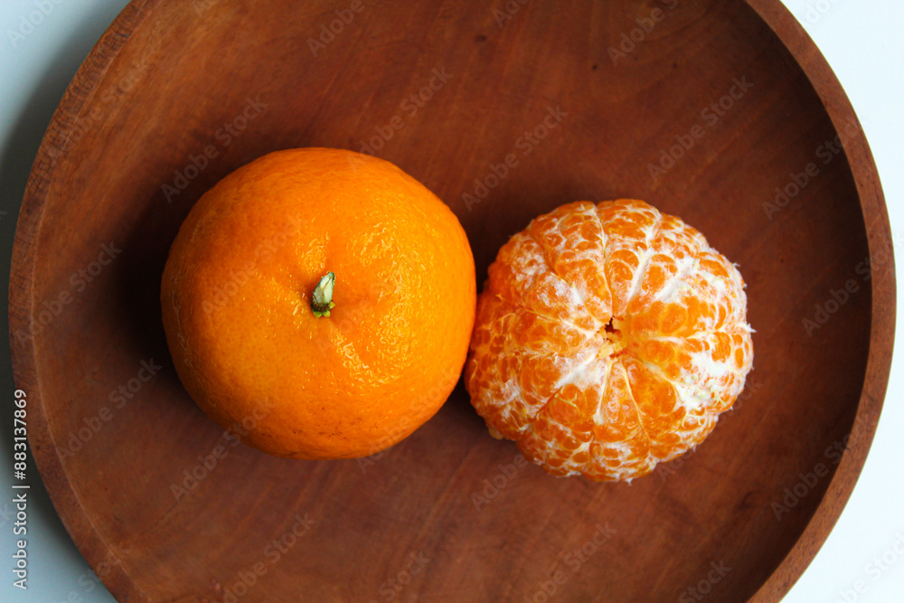 Wall mural comparison of orange fruit before and after peeled, served on wooden plate, flat lay or top view