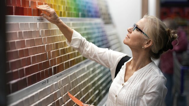 Closeup of smiling mature woman comparing color swatches at a paint display shopping for home redecorating renovation project, in a hardware store. - Powered by Adobe