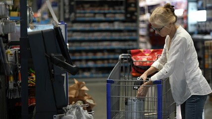 Winchester, VA, USA - 05 14 2024: Happy mature woman at the self checkout in a big box hardware store using hand scanner.
