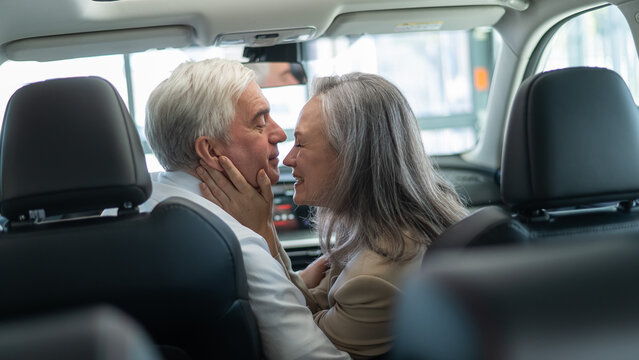 Mature Caucasian couple sitting in a new car and rejoicing at the purchase. 