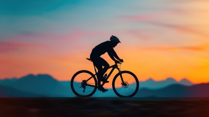 Fototapeta premium Silhouette of a cyclist riding a bike against a colorful sunset sky, with mountains in the background, capturing outdoor adventure and freedom.