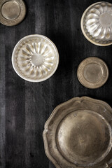 Vintage pewter plates and bowls on black chalkboard background. Flat lay. Top view. Food concept. Dark mood food photography.